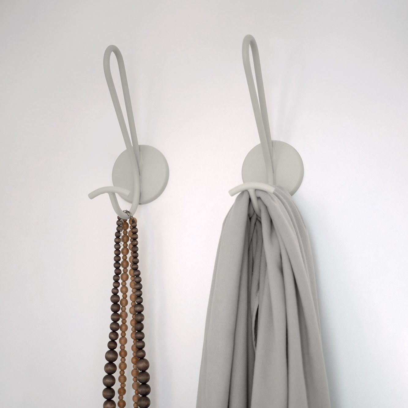 Two wall hooks with a necklace and a scarf on a plain background