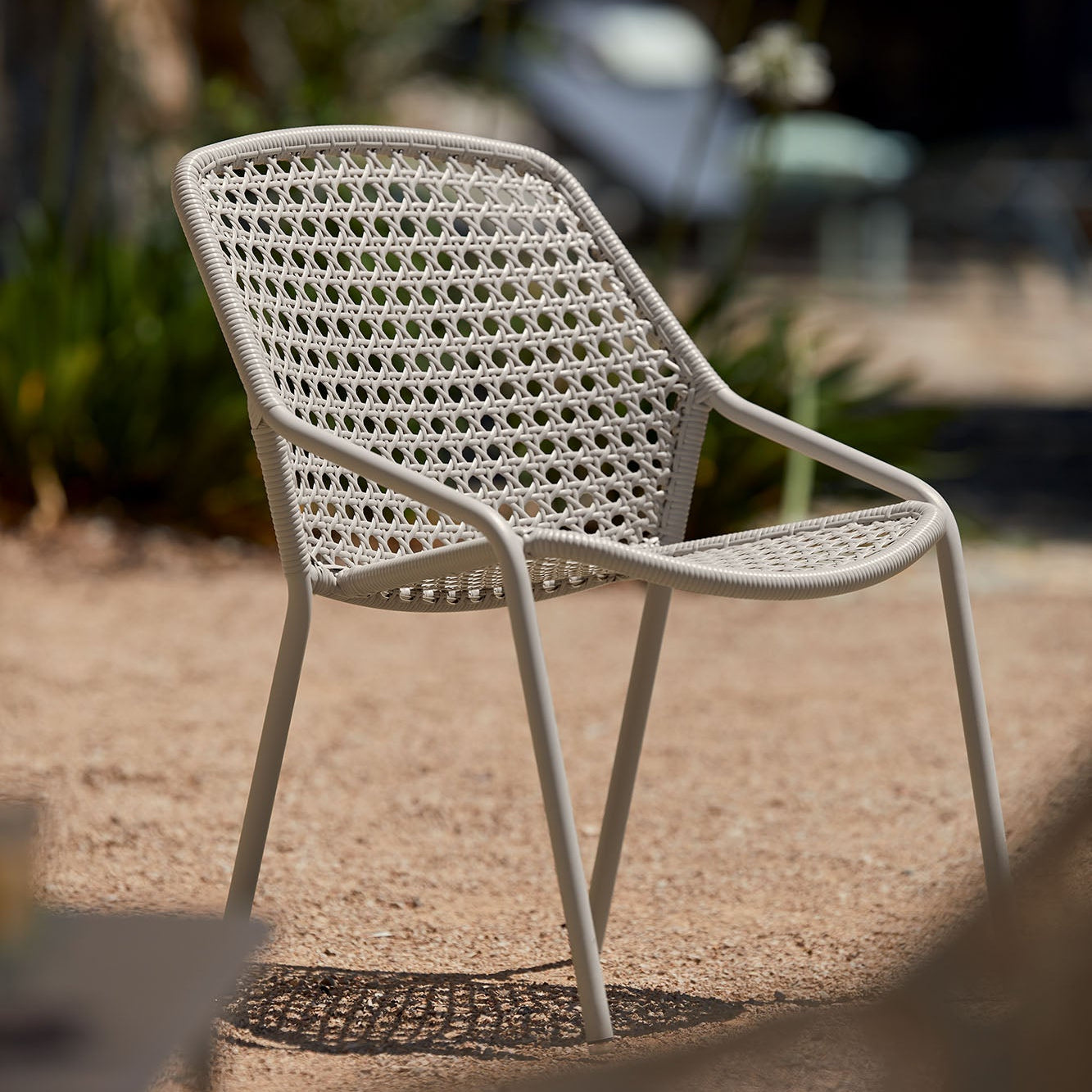 White wicker chair on a gravel surface with blurred greenery in the background