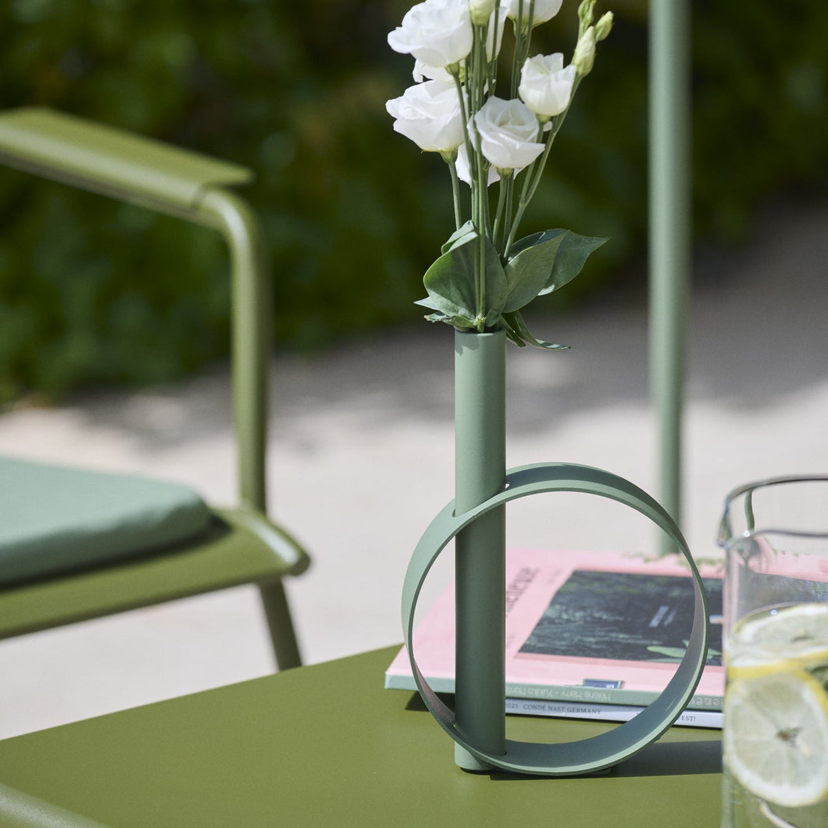 Green vase with white flowers on a green table outdoors