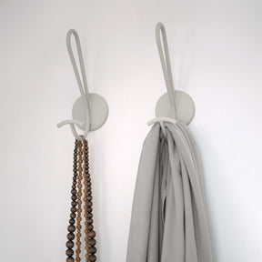 Two wall hooks with a necklace and a scarf on a plain background