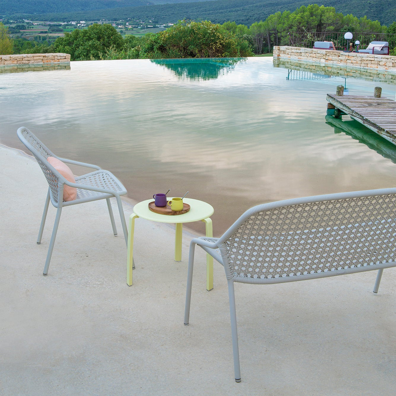 Outdoor patio with chairs and a table by a pool with a scenic view.