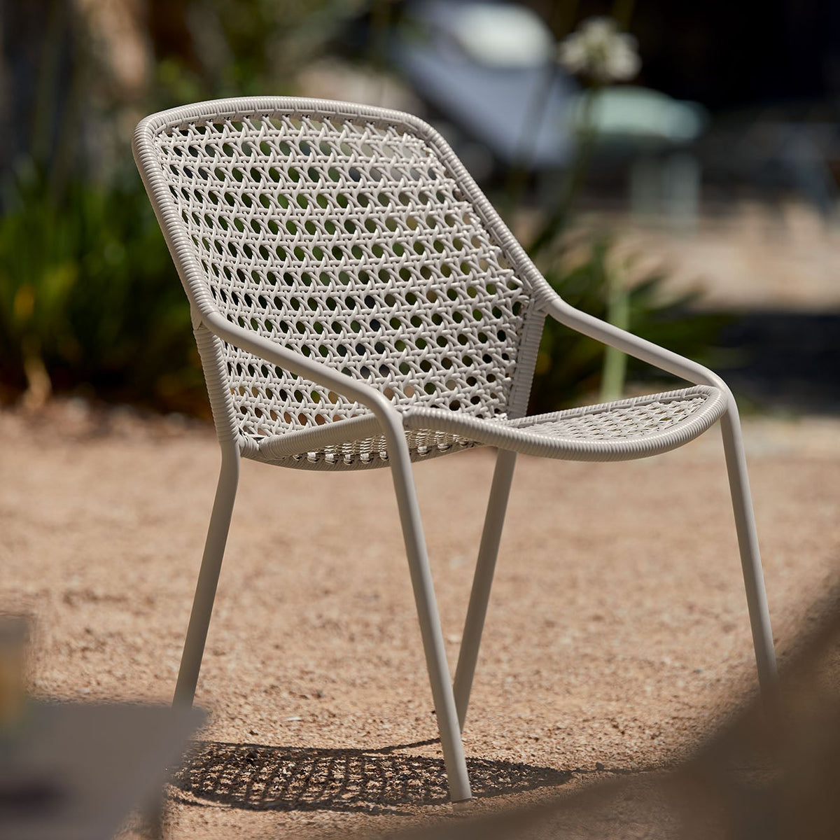 White wicker chair on a gravel surface with blurred greenery in the background