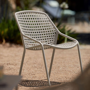 White wicker chair on a gravel surface with blurred greenery in the background