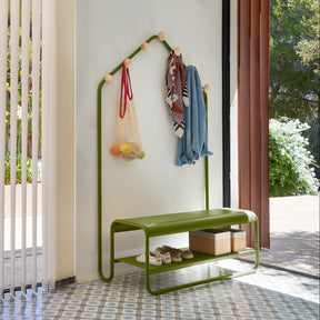 Green metal coat rack with shelves against a white wall outdoors.