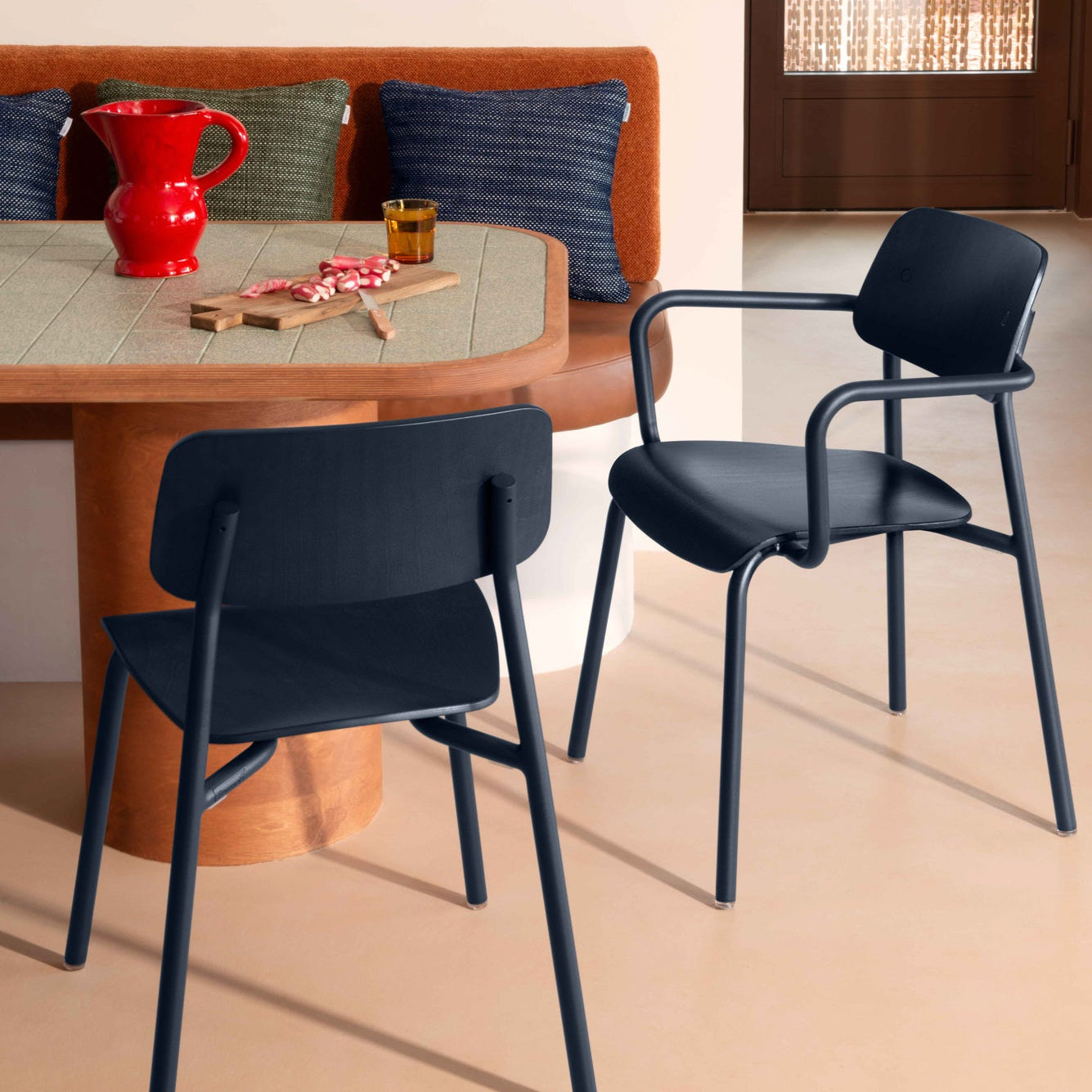 Two dark blue chairs in front of a wooden table with a red pitcher and other items.